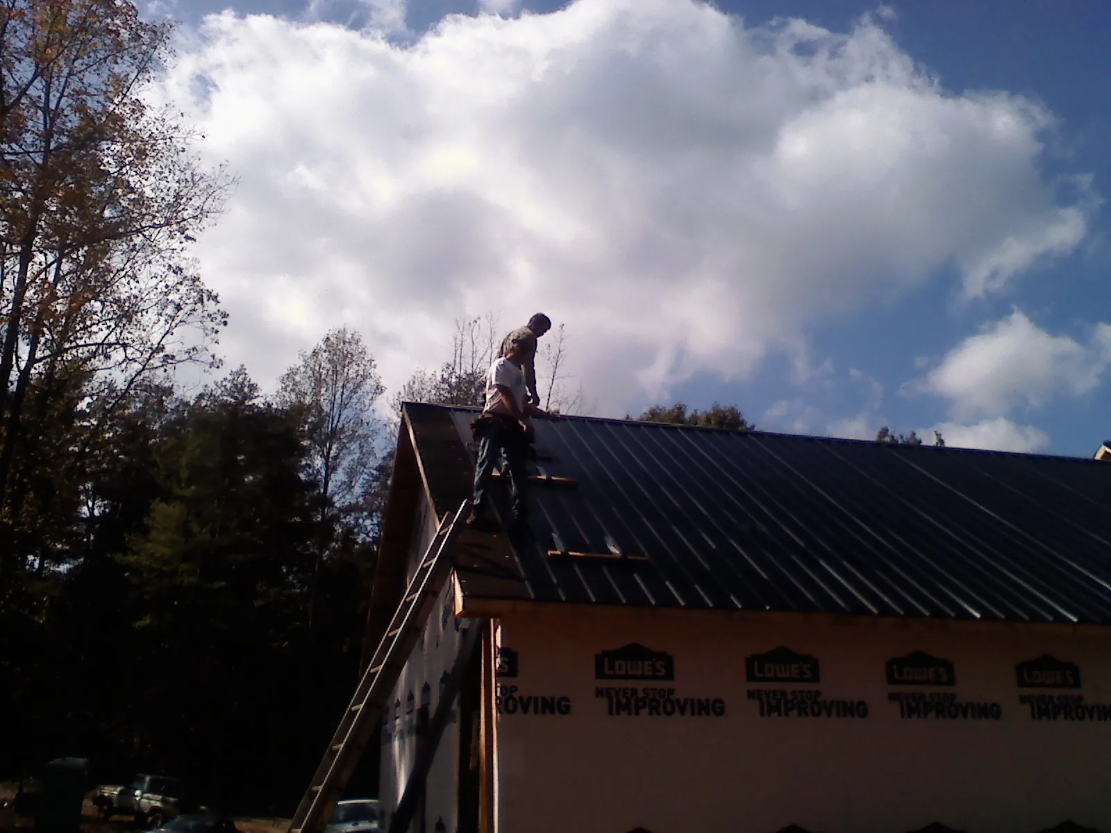 Roofer fastening dark metal panels high against a cloudy sky, from a Roof Inspection job in Danvers