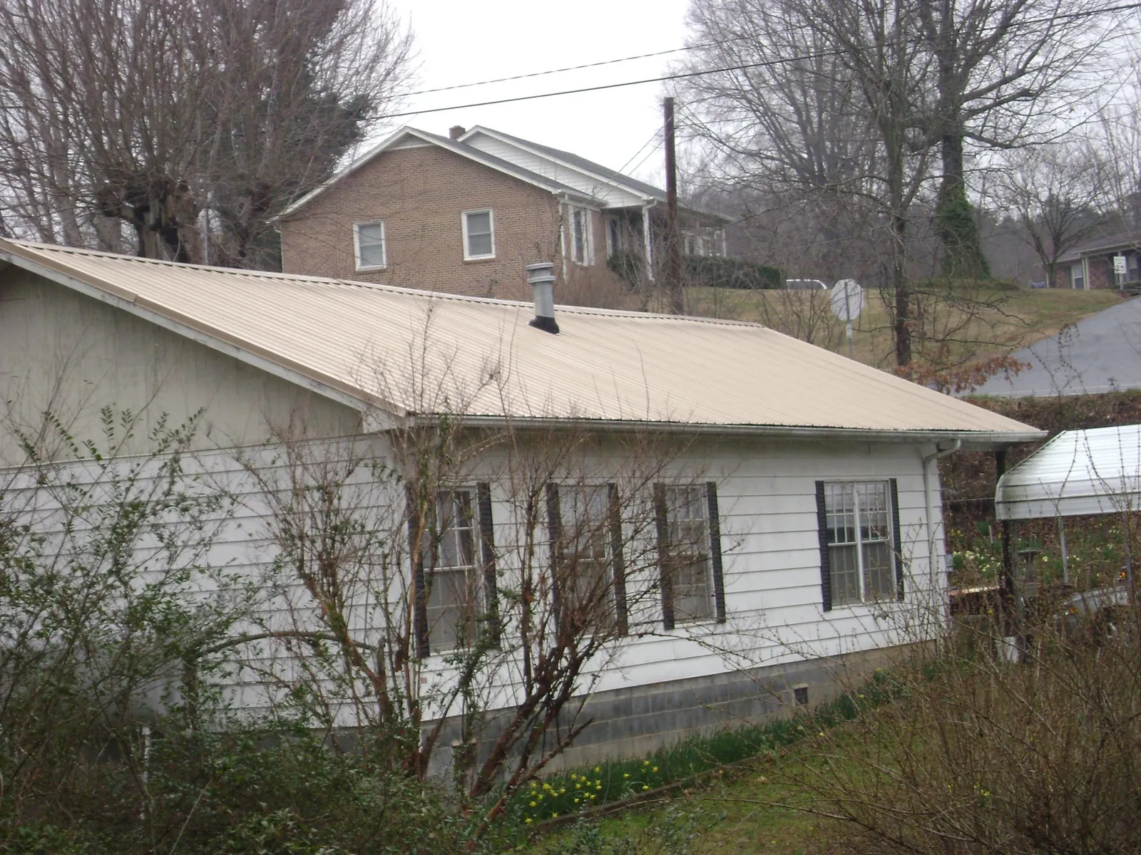 Tan metal roof on a white sided house set into a hillside — Commercial Roofing by Roofing Brothers in Danvers